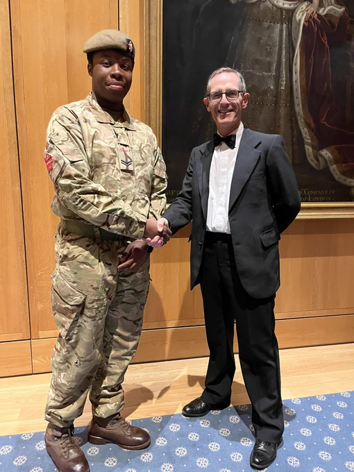Man in a dinner suit shaking hands with a younger man in army fatigues.