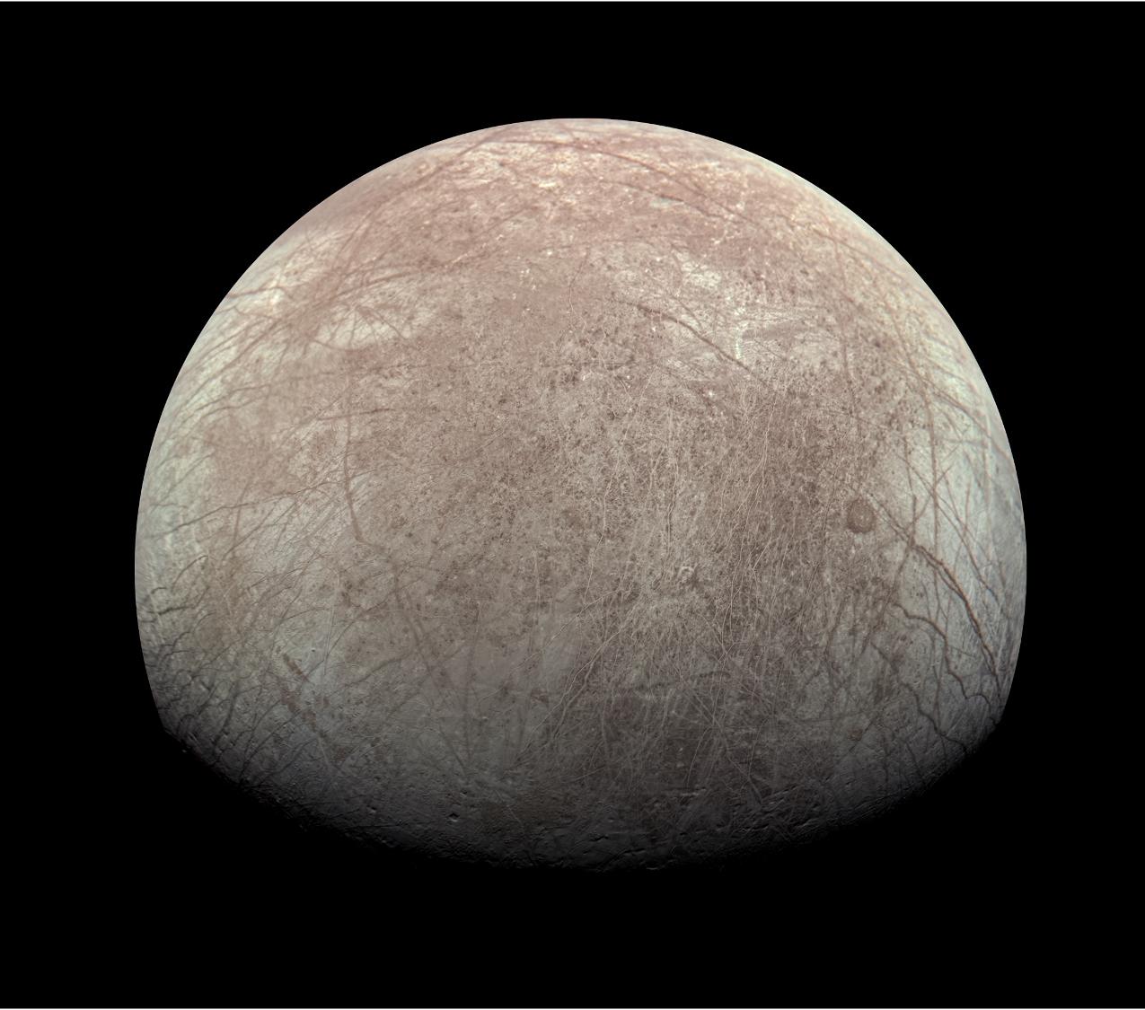 Europa seen against the blackness of space. The moons relatively smooth surface is criss-crossed with cracks and grooves. Image processed from raw JunoCam data by Kevin M. Gill