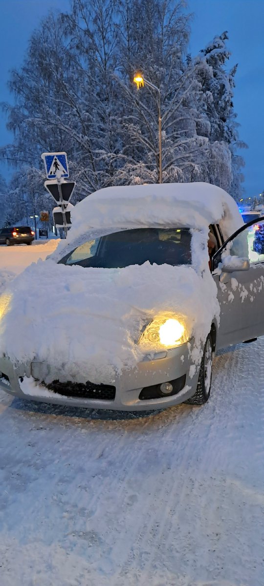 Lumeen peittynyt auto etuvalot päällä ja ovi auki.