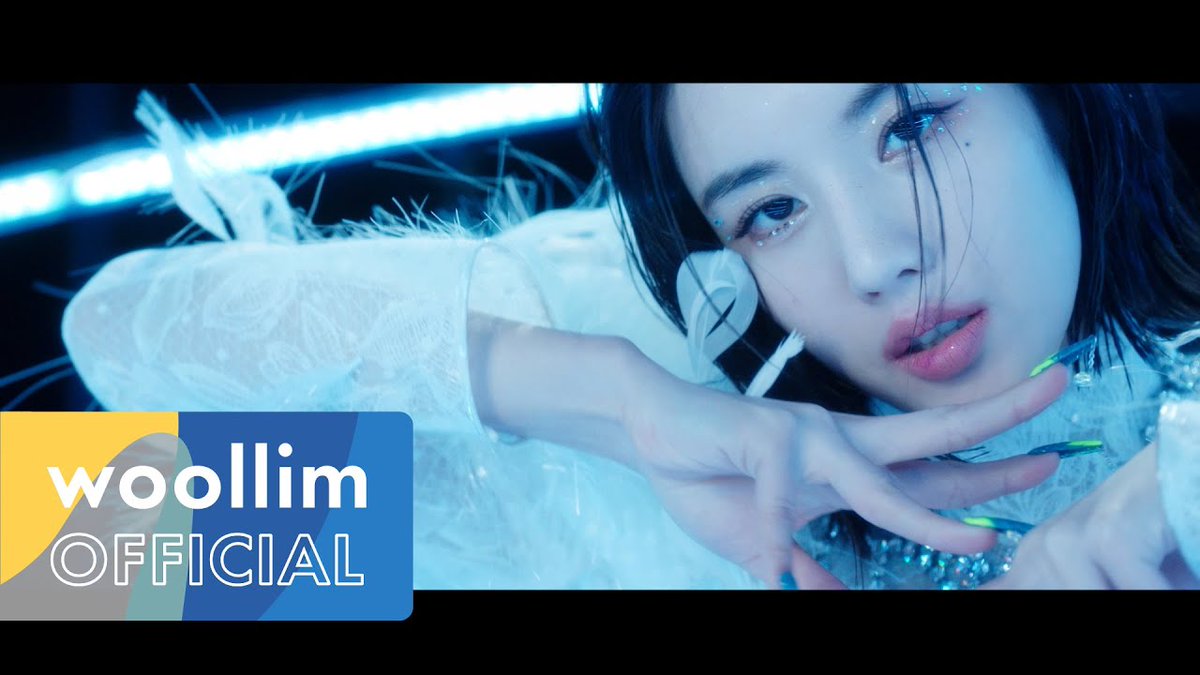 Close-up of a woman with dark hair, dramatic eye makeup, and green nails in a cool blue-lit setting, with a 'woollim OFFICIAL' logo in the lower-left corner.