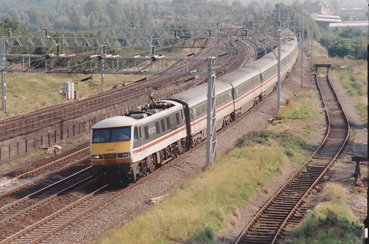 Today’s archive photo… it could be 2022 and <a href="/InterCity86101/">InterCity</a> Friday Charter… but it’s the late 80s and an unidentified 90 sweeps past the entrance to Wolverton Works with a northbound service