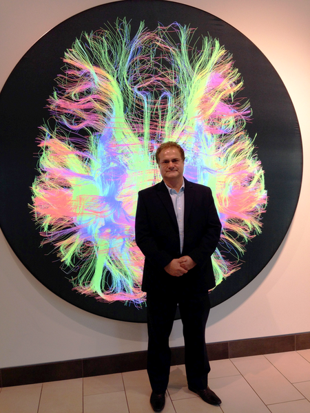 A picture of Prof Zoltan Molnar stood in front of a multicoloured picture of the brain.