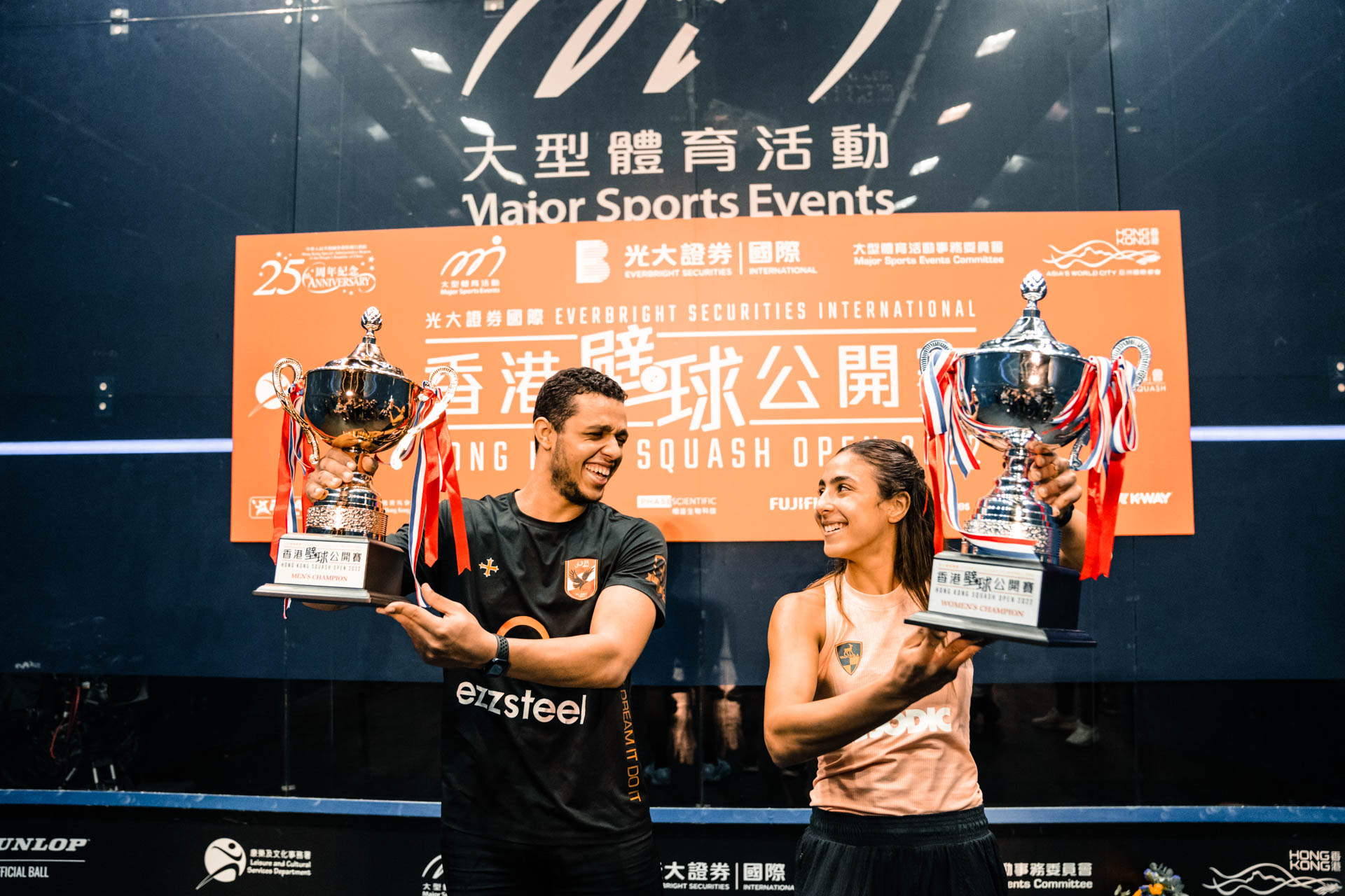 Mostafa Asal and Hania El Hammamy lift the Hong Kong Open trophies and smile at each other 