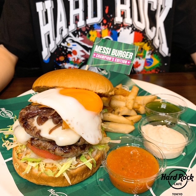 hrc_tokyo's tweet photo. MESSI BURGER CHAMPION'S EDITION⚽スペシャルバージョンとして、3種のオリジナルソースを加えてバージョンアップ!ジューシーなダブルパテ、モッツアレラチーズ、ソーセージ、トマト、レタス、目玉焼きが乗ったボリューミーな一品🍴
豪快にかぶりついちゃって!
#LetsGetMessi #MessiBurger https://t.co/Q1YZJ1q3I4