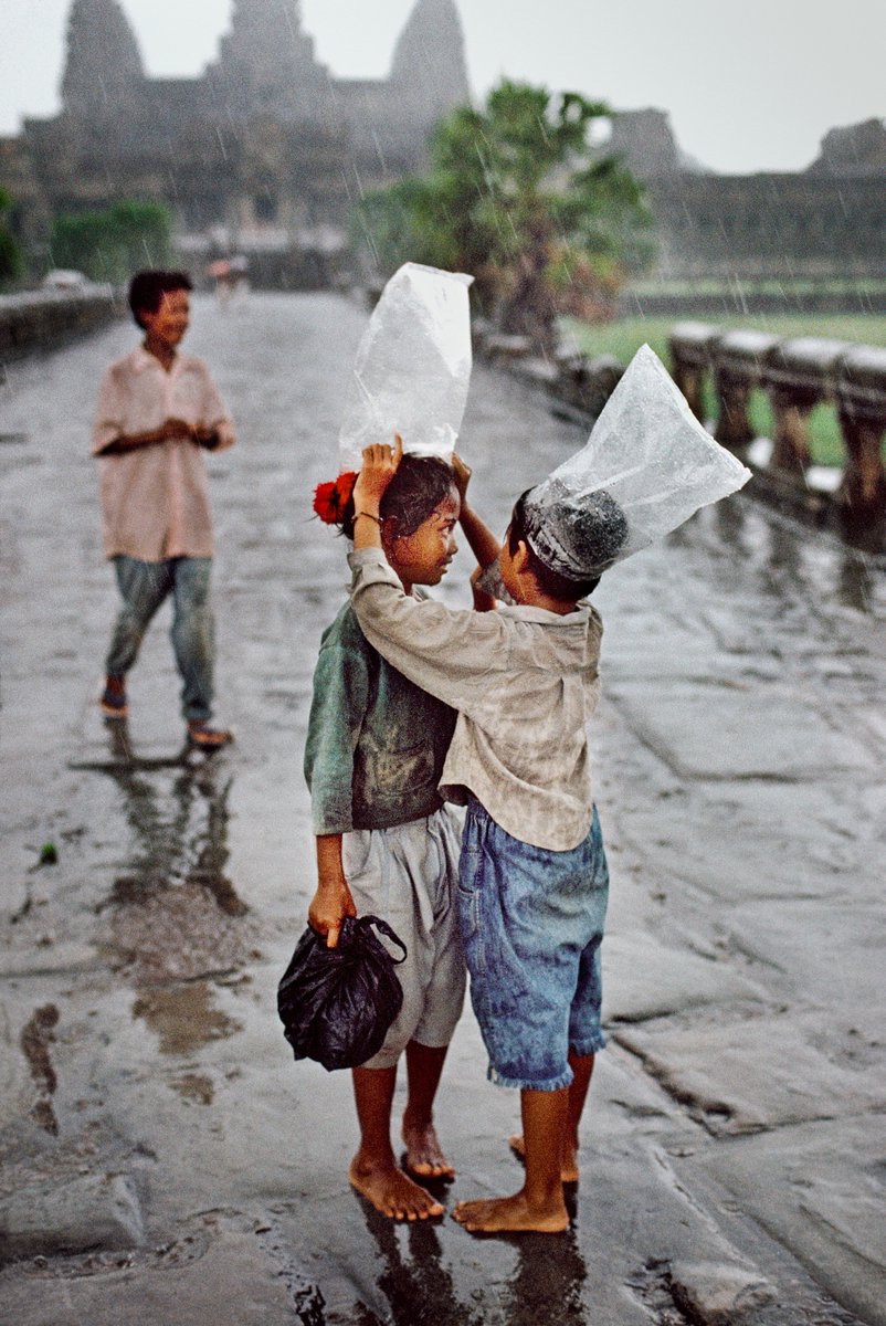 Children use plastic bags as improvised umbrellas, Angkor Wat, Cambodia, 1998.