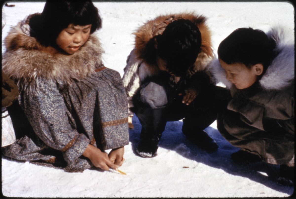 ANC_Historian's tweet photo. Dec 1965 Newtok, three children playing together. The girl is using a story knife--a yaaruin in Central Yup'ik--to draw in the snow, part of a game or story. Via Anchorage Museum. #alaskahistory #newtok https://t.co/0WFPsmgHhk