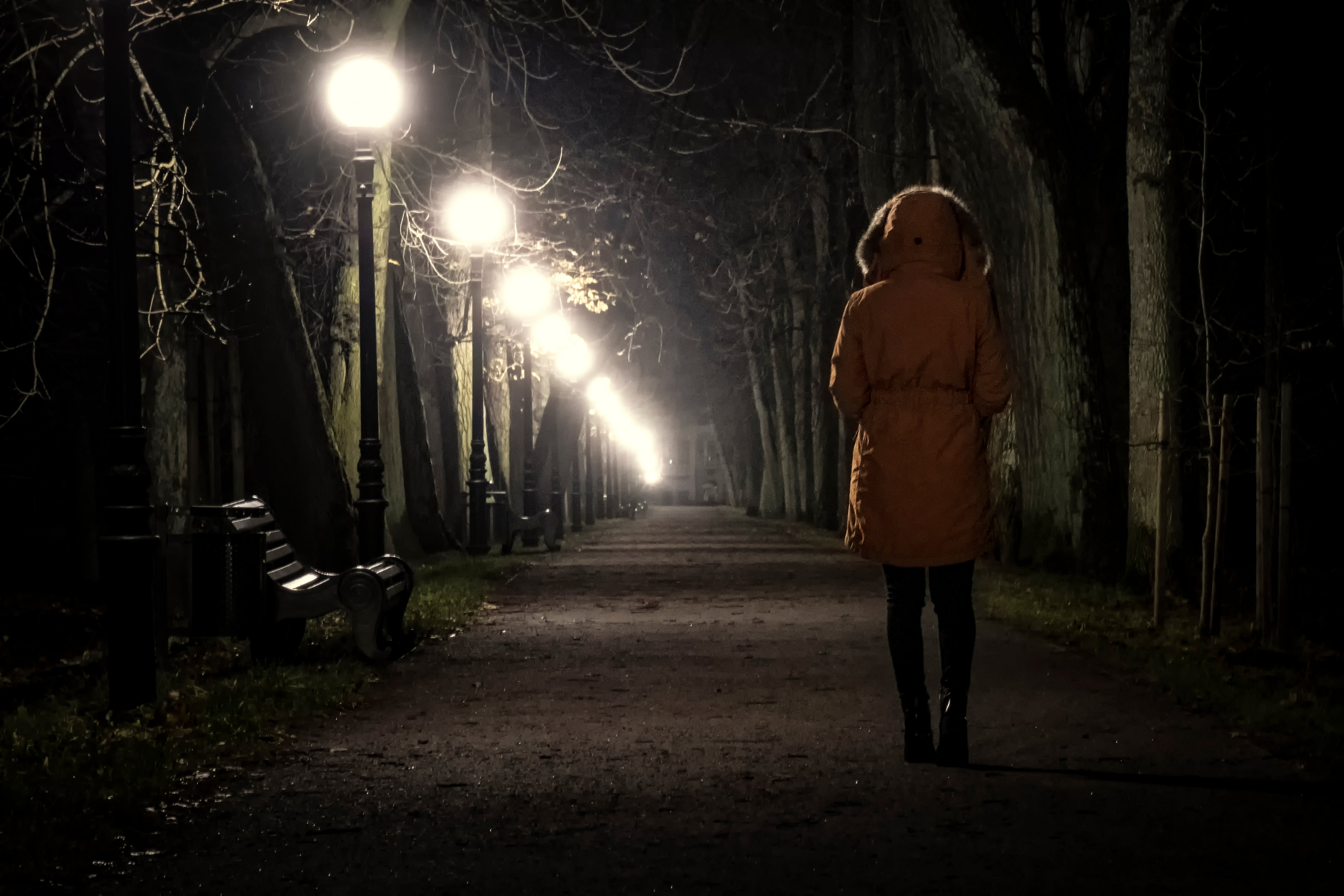 A photograph of a woman walking through a park at night