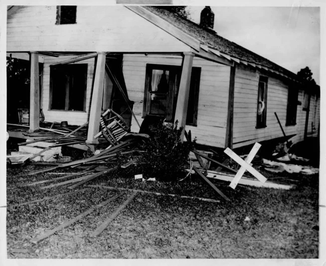 White house with windows destroyed and wood or siding strewn on ground.