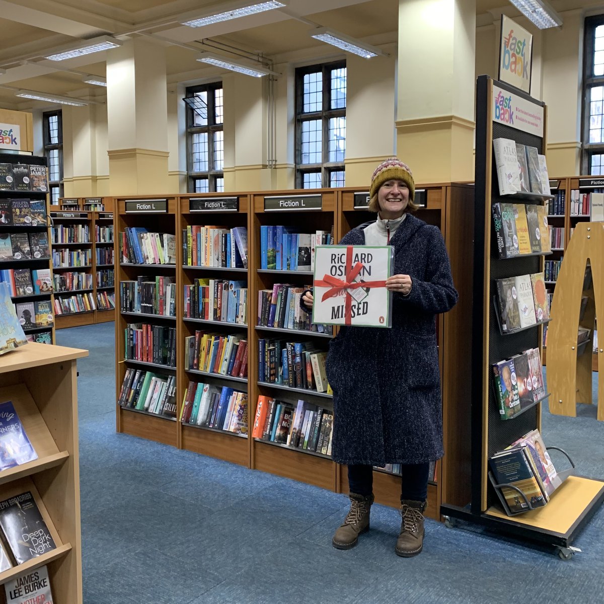 Competition winner holding vinyl record wrapped with red bow, standing in front of bookshelves at Bristol Central Library