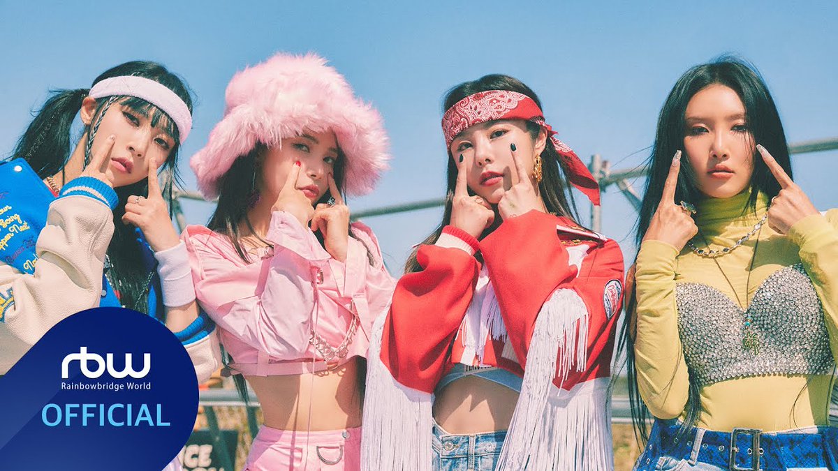 A K-pop group photo featuring four female performers posing with middle finger gestures in colorful streetwear, with a 'Rainbowbridge World (rbw) OFFICIAL' logo in the corner.