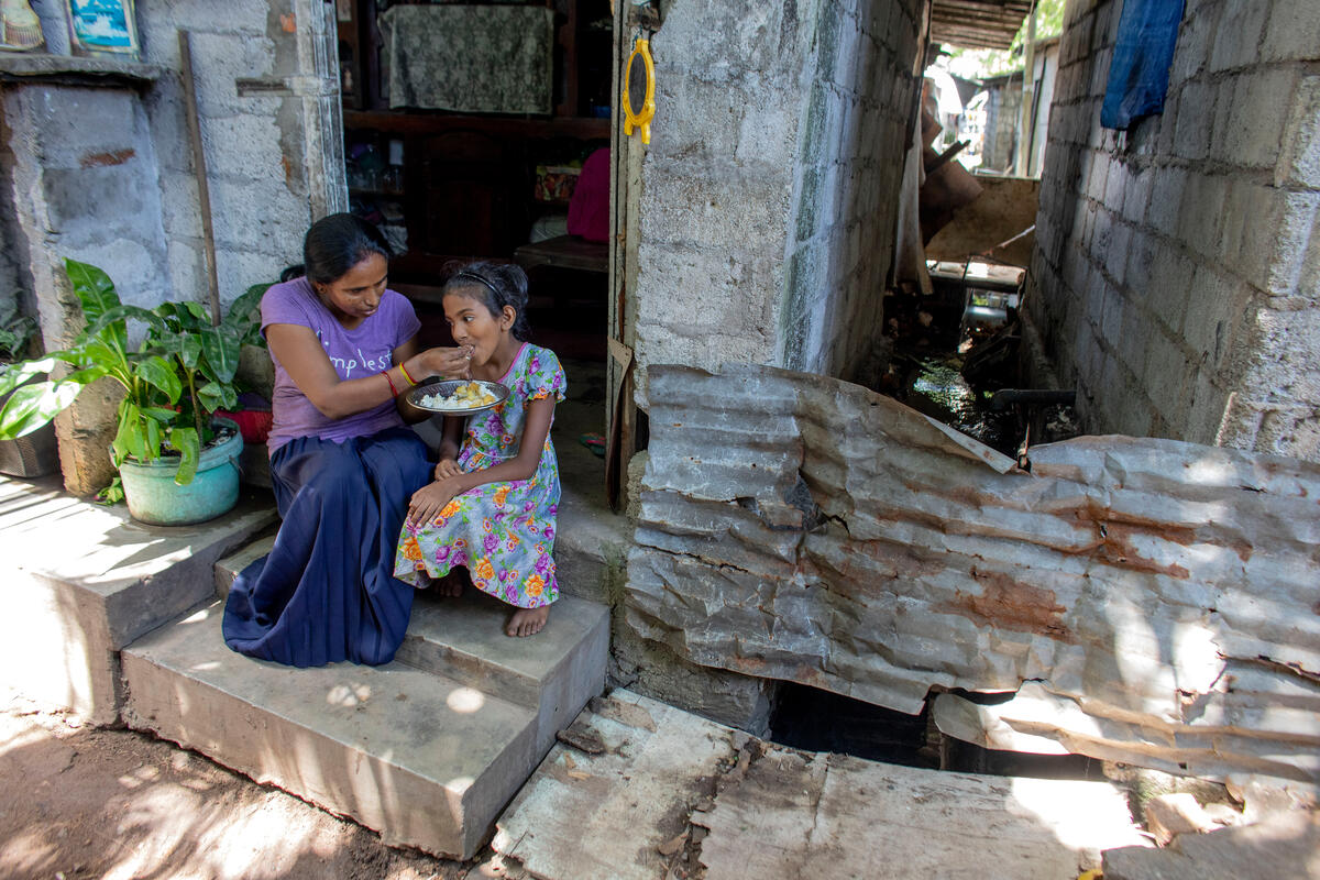 Minabige, 49, feed her daughter Darhika, 9, on the steps of their home in Sri Lanka. With her husband and two daughters, the family of four live in a cramped one room shack. Amid the economic crisis, women and children from poor rural and urban households who rely on national social safety net programmes have been left without help.
