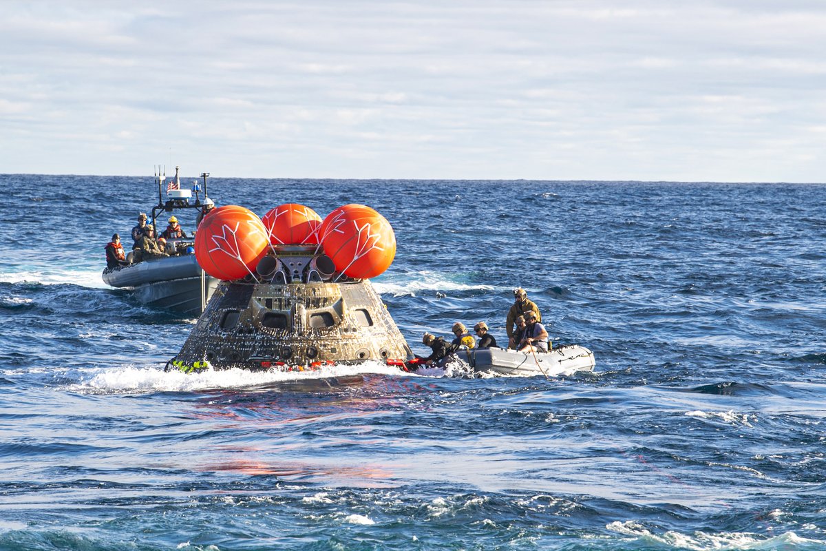 DeptofWar's tweet photo. Splashdown salvagers. 
@USNavy divers rig the @NASA Artemis I Orion spacecraft to a device to pull it into the well deck of the USS Portland. The operation was part of a DoD effort to determine best practices for safely retrieving spacecraft capable of carrying humans. https://t.co/K9bRGIlail