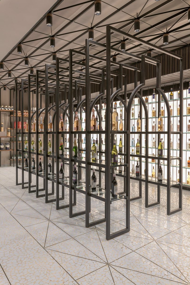 A walkway featuring a series of bottle-shaped frames occupies pride of place in the narrative of the wine shop. It invites the user inside it and guides them into one of the sections. A fun touch in an otherwise contemporary, straight-laced narrative. #interiordesign