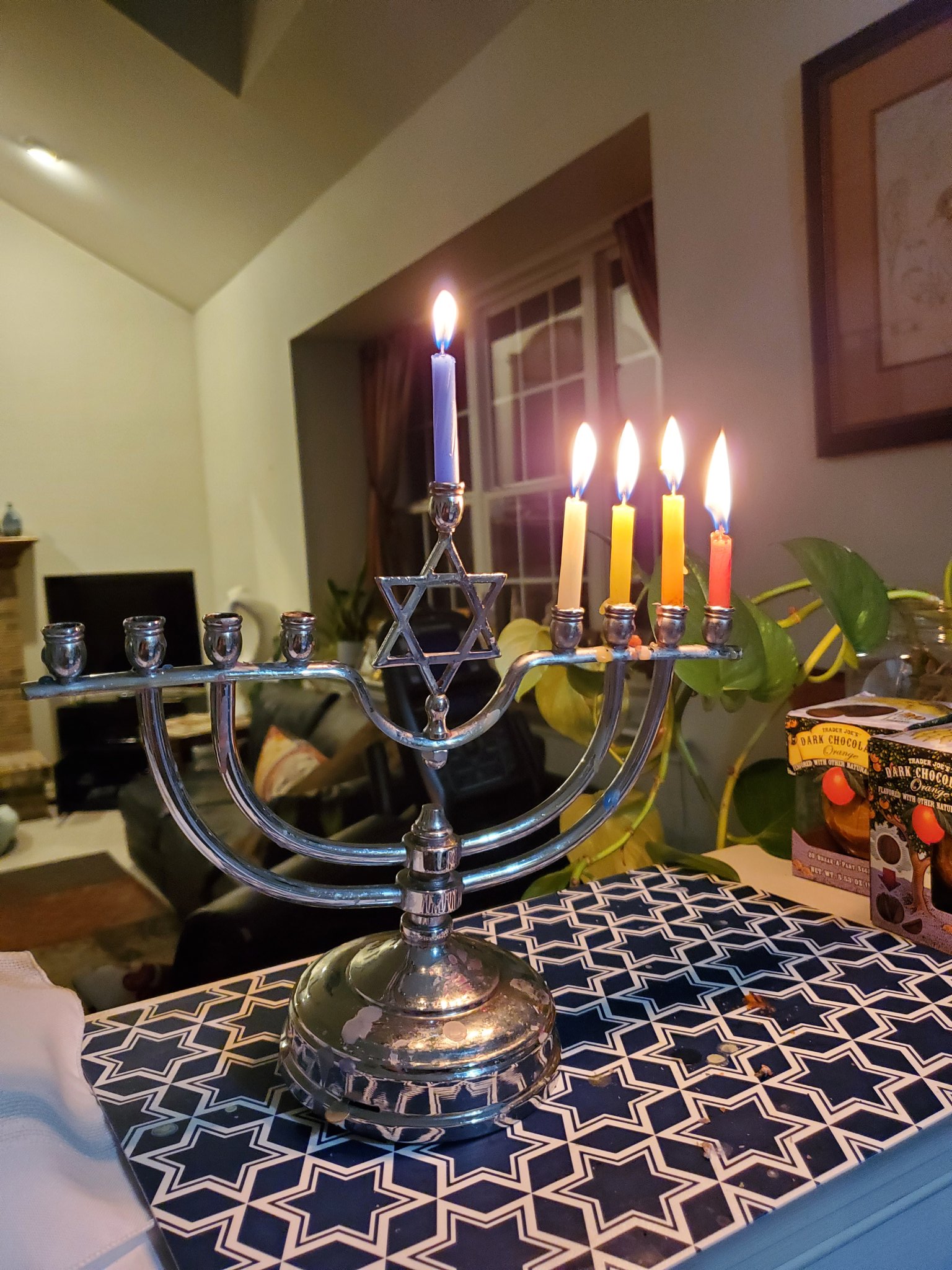 A silver menorah that has a Star of David in the center with 5 candles lit for the 4th night of Hanukkah