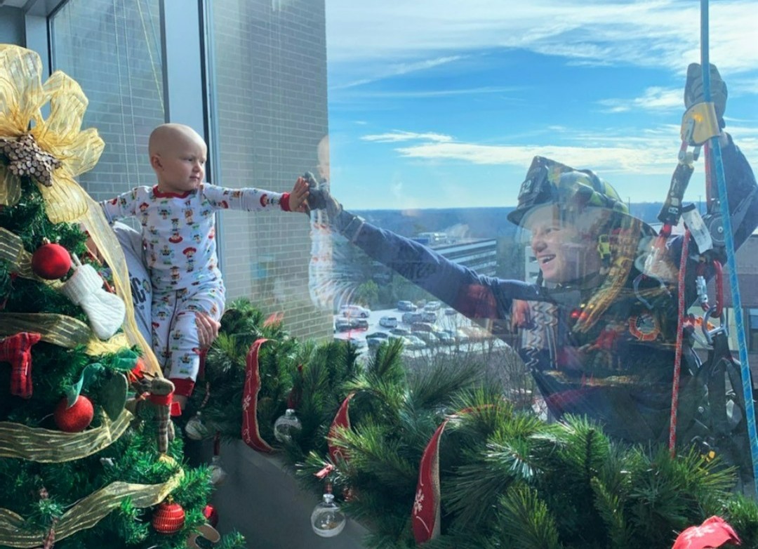 childrensatl's tweet photo. May this holiday season bring you many reasons to smile… like this touching moment. 😍 Hand to hand, little Levi locked eyes with a local firefighter as he was propelling down our hospital building, spreading some holiday joy to our patients. #happyholidays https://t.co/New7BH5XGr