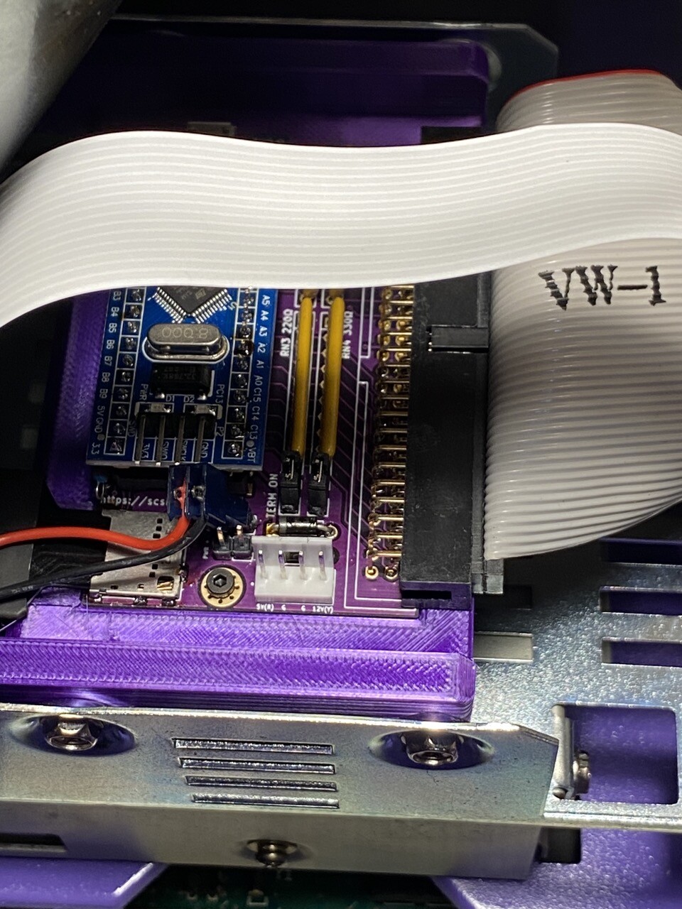 A purple PCB BlueSCSI affixed to a purple bracket mount that’s screwed into the hard drive sled of the SE/30