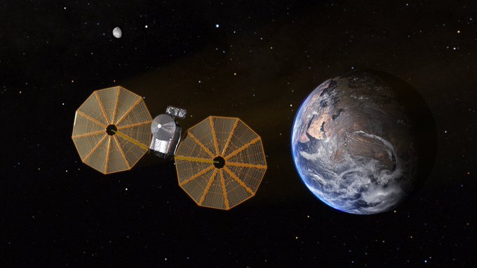 Graphic of Lucy spacecraft in space with the Earth and Moon in the distance and stars in the background. The spacecraft has two large, round solar arrays on either wide of the body.