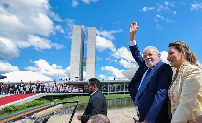 Lula em cima do carro em direção ao Congresso, ao lado de Janja. Ele acena para o público.