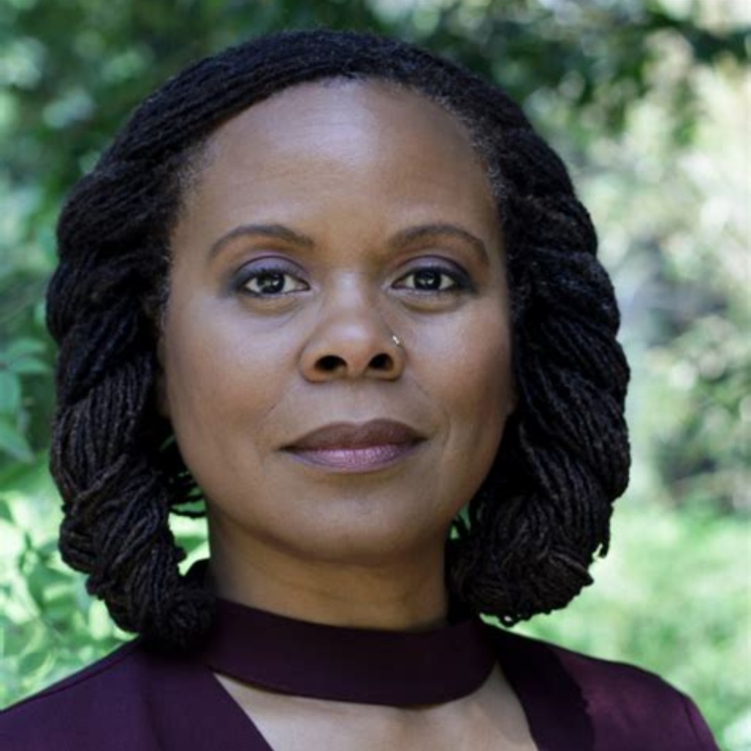Outdoor headshot of Chandra Ford in a deep purple top staring directly at the camera
