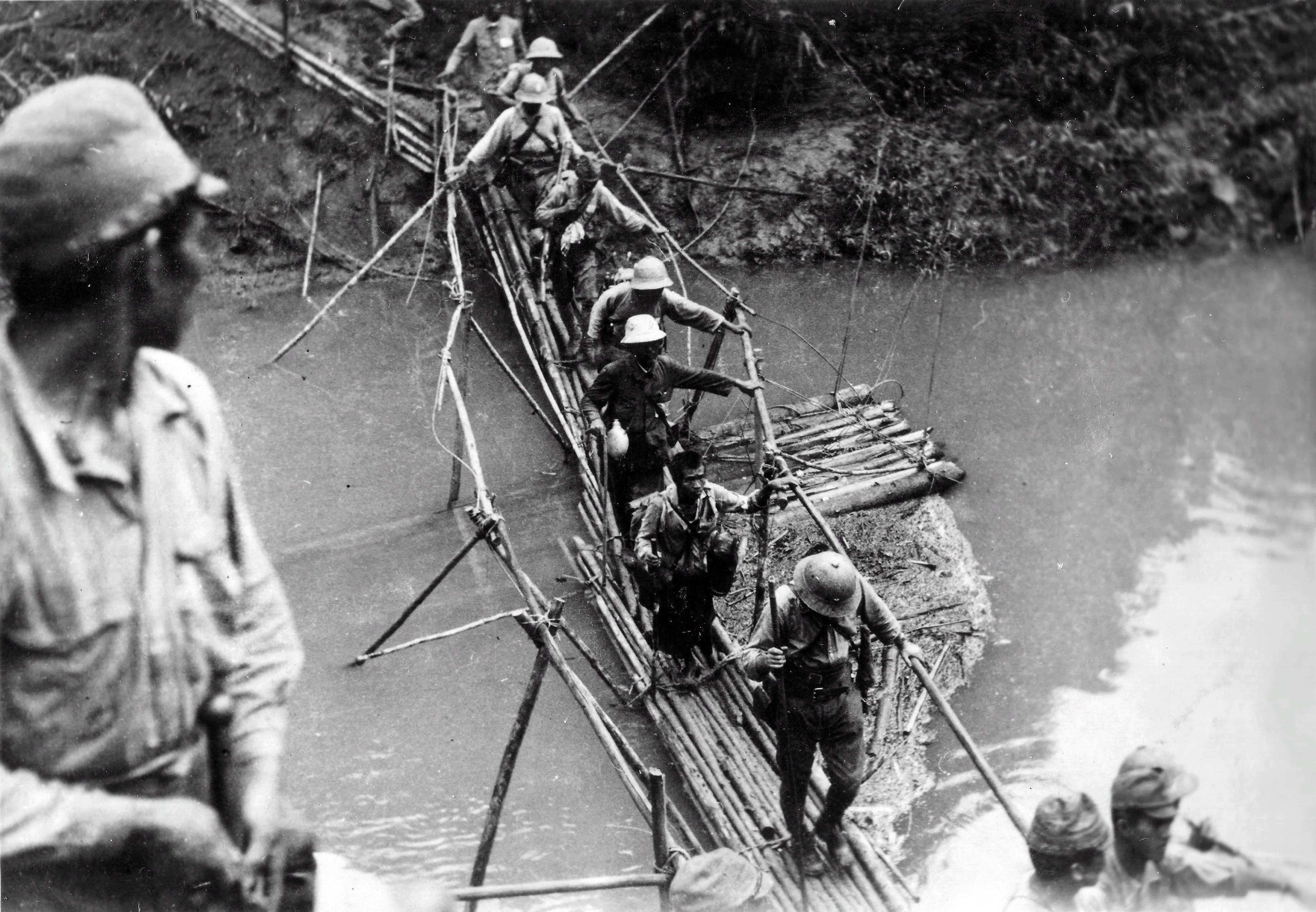 Japanese infantry unit crosses the bridge over the river in the jungles of Burma