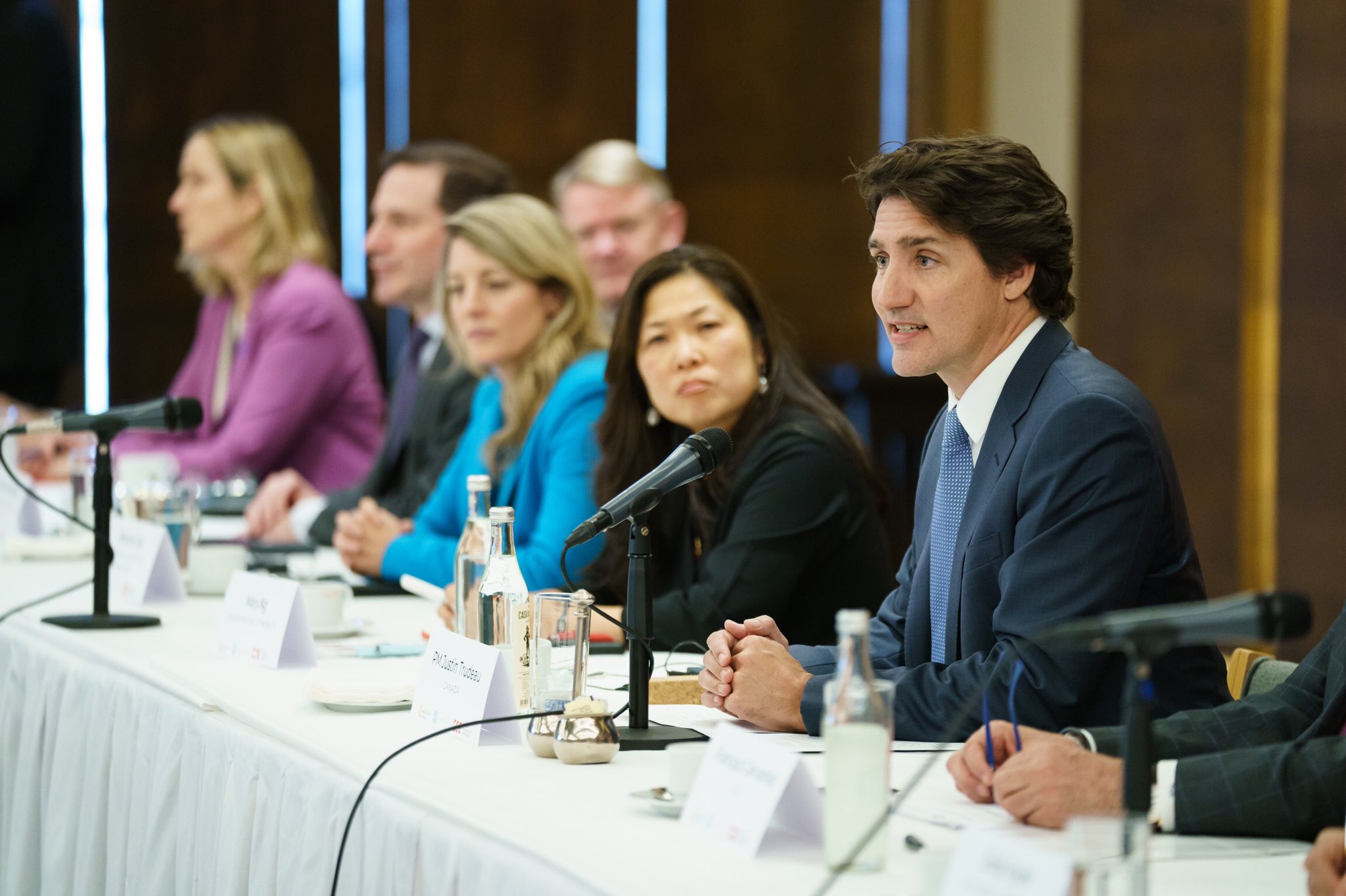 Le premier ministre Justin Trudeau est assis à une table et parle au micro. Les ministres Mary Ng, Mélanie Joly et Marco Mendicino sont assis à côté de lui. L'ambassadrice Kirsten Hillman et l'ambassadeur Graeme Clarke sont aussi assis à côté de lui.