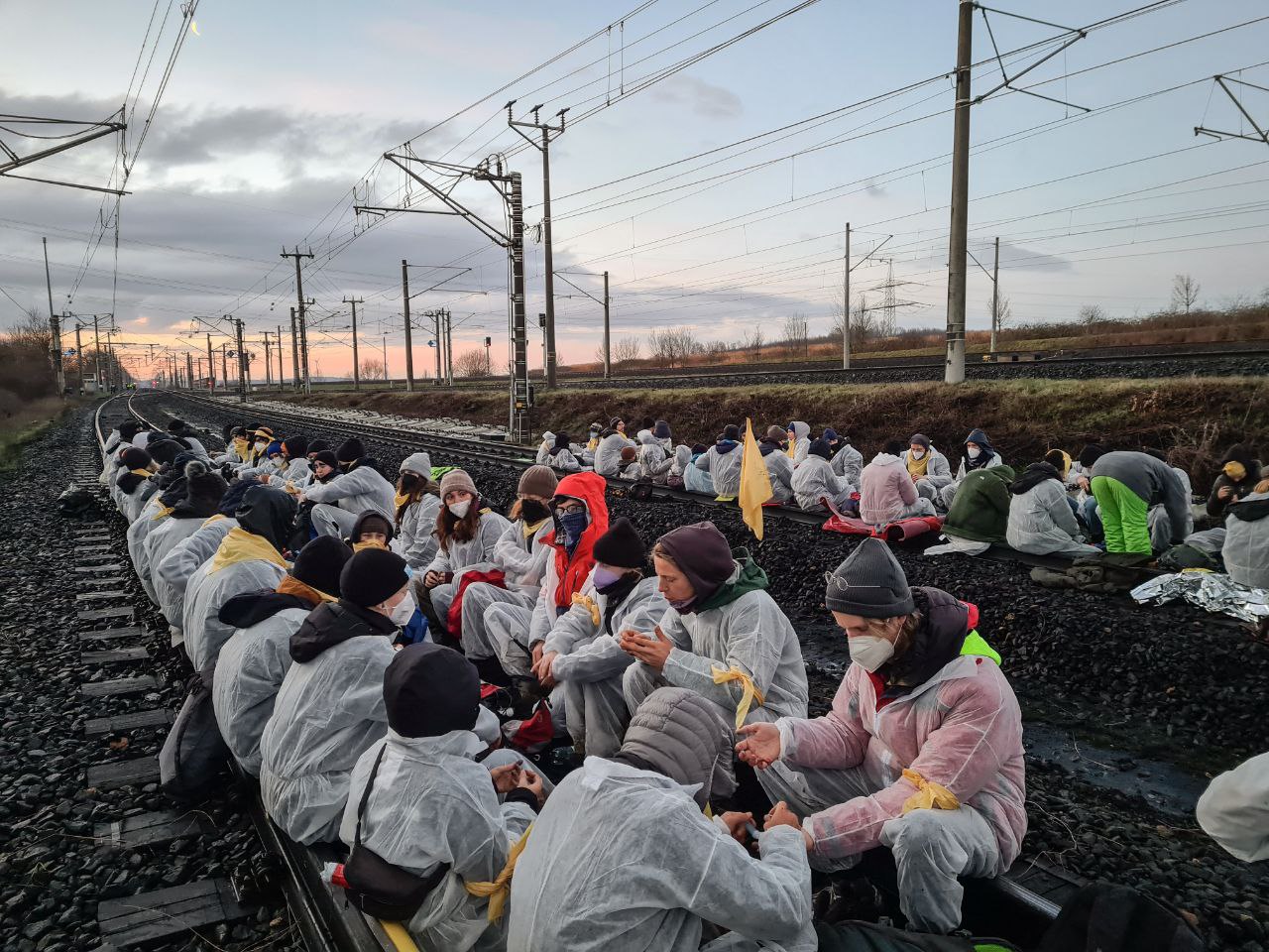 Ende Gelände Aktivisti sitzen in in 4 reihen auf zwei gleisen. am horrizont der sonnenaufgang