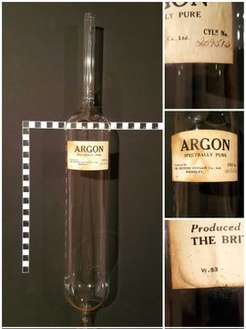 Photo of an old cylindrical glass ampoule of argon, produced by The British Oxygen Company Limited, labelled "spectrally pure". The cylinder is approximately 33 cm long and 8 cm in diameter. It's pinched off and sealed at the bottom while at the top end is a 2 cm diameter glass tube about 15 cm long. Inside that tube is a breakseal, designed to be broken by a magnet to release the contents of the ampoule into a vacuum/gas handling system to which the open end of the 2 cm tubing would be sealed for use.