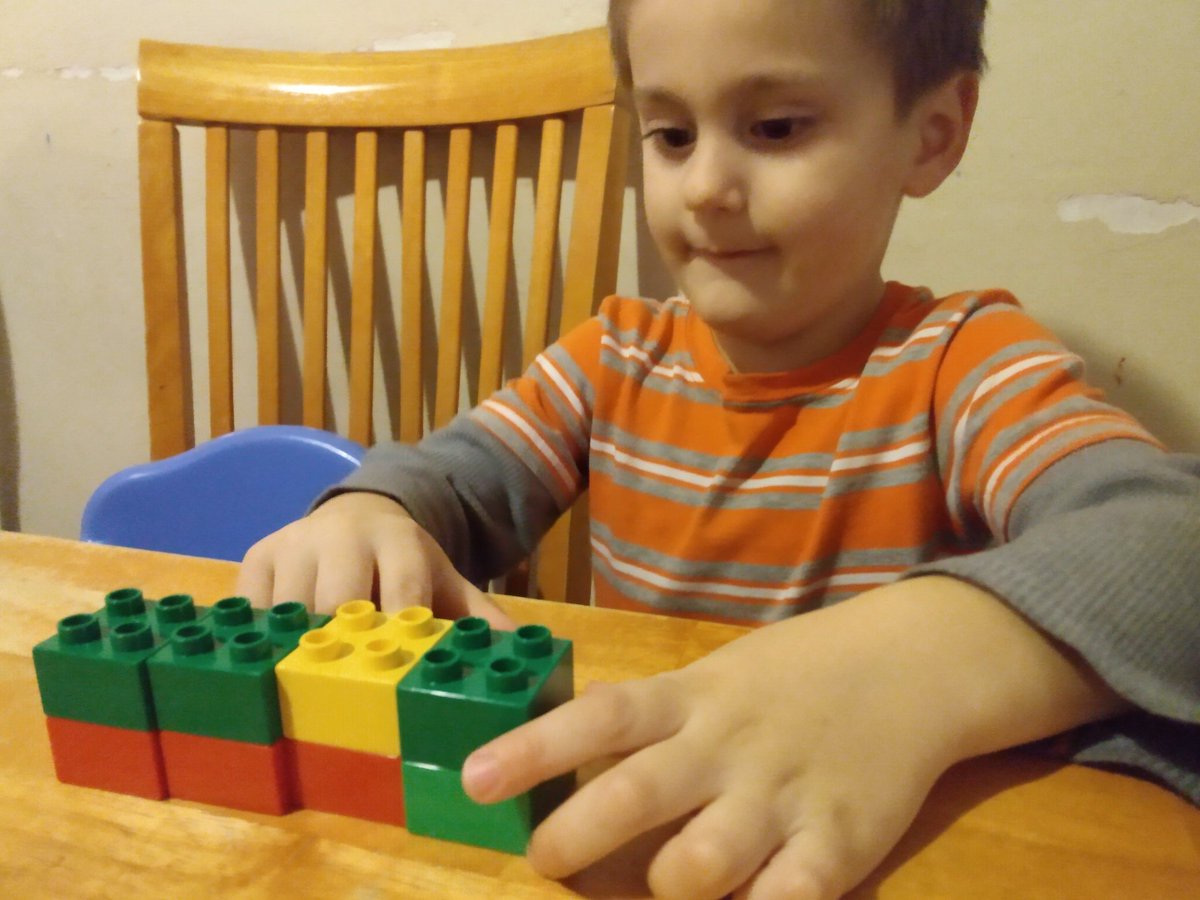 Nathan (age 3) at the table with four stacks of Duplos, each two blocks high. He has them lined up in a row and he's counting while pointing with his finger.