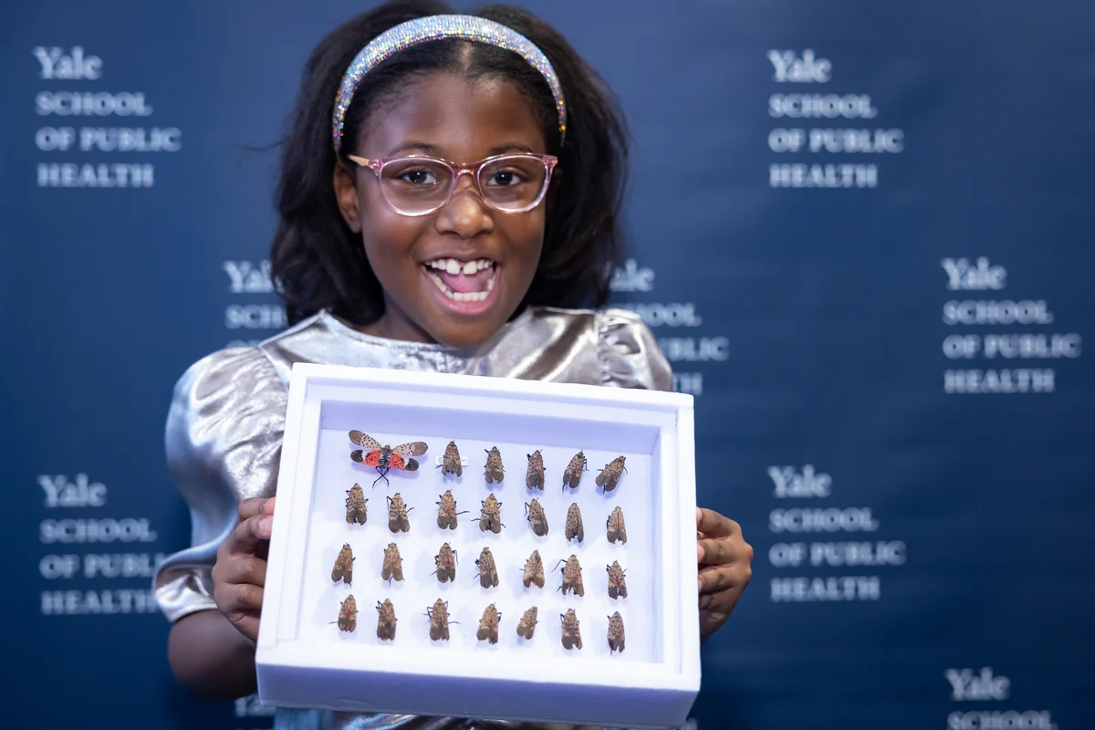 Bobbi Wilson holding framed lanternfly collection in front of Yale School of Public Health backdrop
