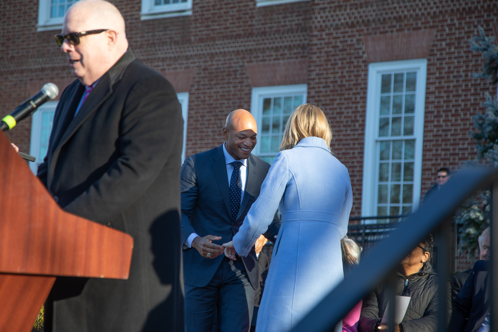 Brooke and Wes Moore share a greeting while Larry Hogan speaks at the podium. 