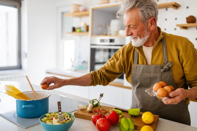 Healthy elderly man smiling whilst cooking healthy food in kitchen