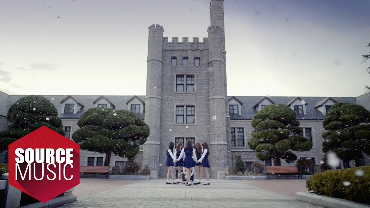 A group of girls in matching navy and white outfits stand in a circle holding hands in front of a large stone castle building with 'SOURCE MUSIC' logo visible.
