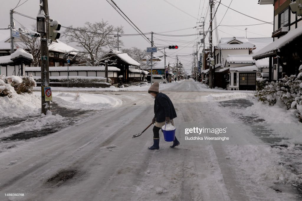 A woman removes snow along a street in Tambasasayama, #Japan. According to reports and the Japan Meteorological Agency, temperatures are expected to drop significantly to levels seen only once in a decade. 📸: @buddhikajapan