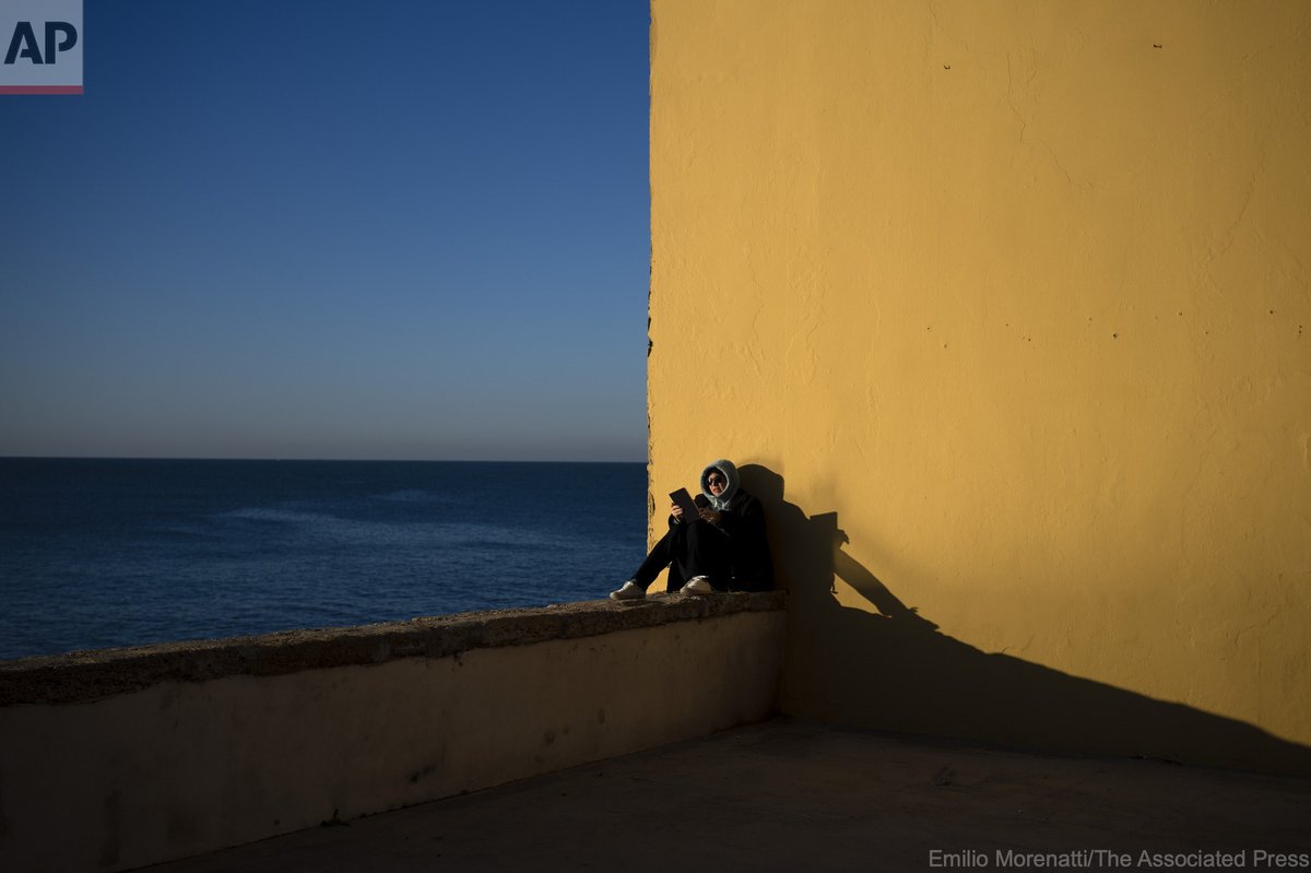 A woman reads by the sea while the first rays of sunlight fall on the city of Cadiz, Spain, Friday, Jan. 27, 2023.