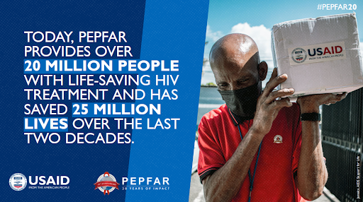 A man carries a box of HIV treatment. The box has USAID branding on the front of it. The text reads, “Today, PEPFAR provides over 20 million people with life-saving HIV treatment and has saved 25 million lives over the last two decades.”