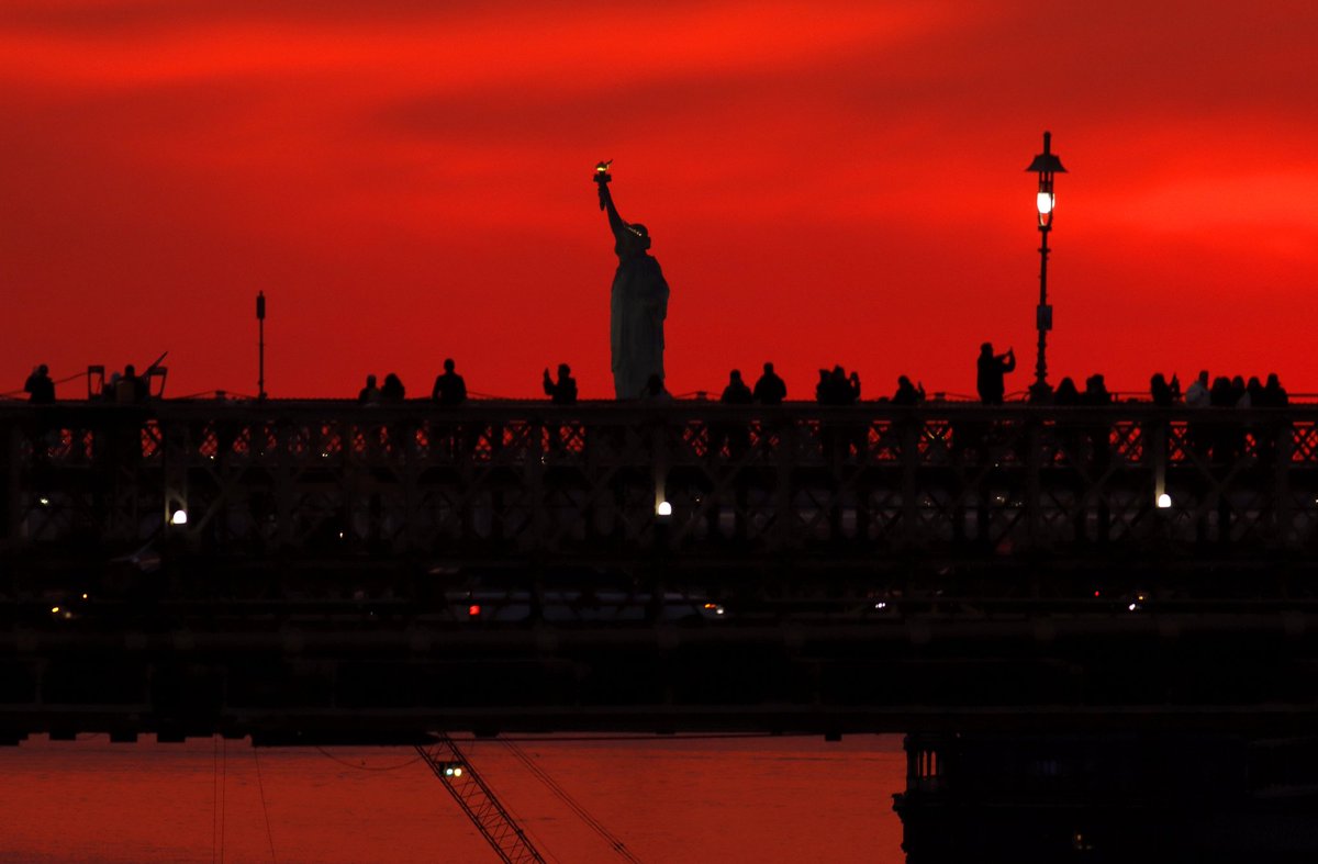GaryHershorn's tweet photo. People on the Brooklyn Bridge as the sun sets behind the Statue of Liberty in New York City, Saturday evening #nyc #newyork #newyorkcity @agreatbigcity @statueellisnps #statueofliberty #sunset @statueellisfdn https://t.co/e7DWbMEvsk