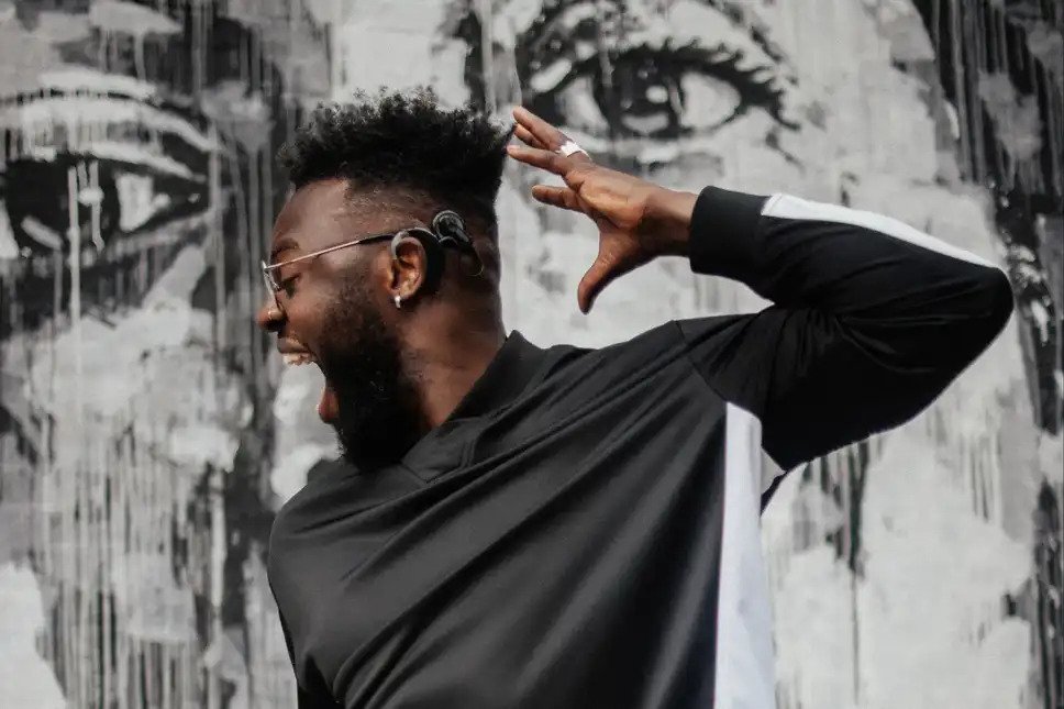 Dancer Chris Fonseca performing, he is a Black man wearing glasses, his head is turned to show his cochlear implant.