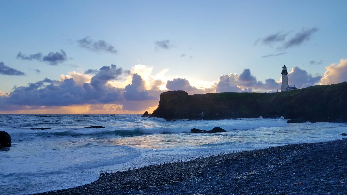 A headland juts out into the ocean with the beach below. A white lighthouse sits on the headland.