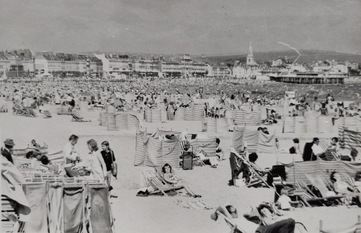 SeasideFerry's tweet photo. A busy day on #Weymouth sands, probably #1960s. The people in charge of deck chair and windbreak hire are doing a roaring trade while their punters just sit and recline in the sunshine. In the background is the bandstand #pier. 
#SaturdaySnaps https://t.co/YTEnMEUaR9