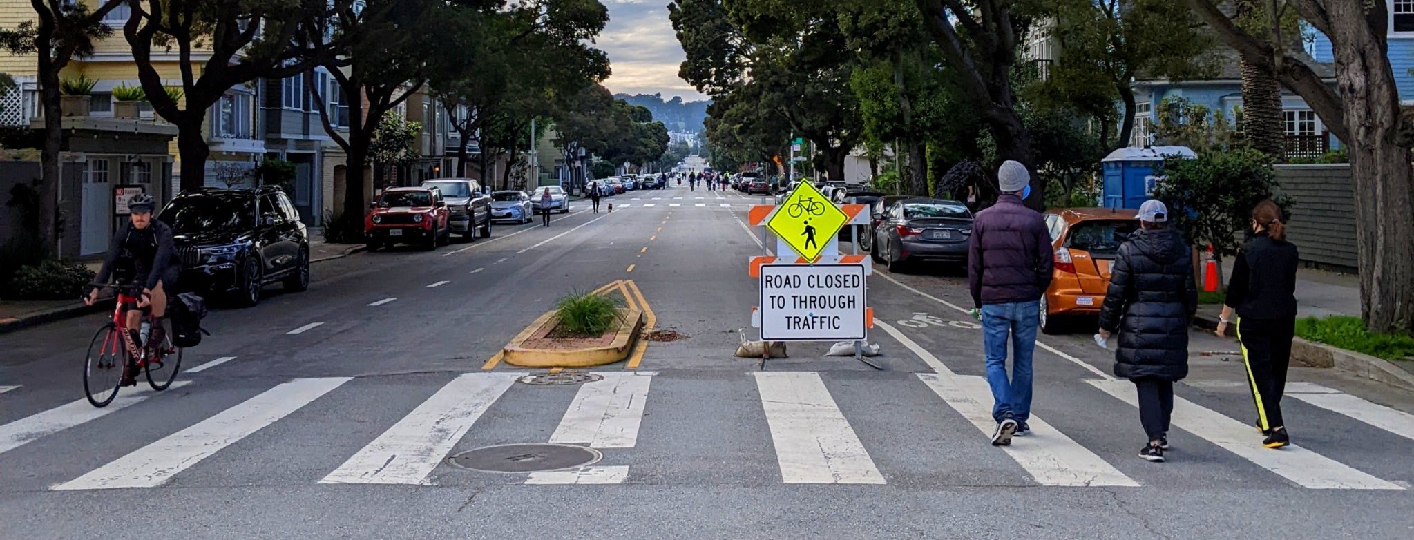 Photo of Slow Lake Street with its original signage/infrastructure, including a “Road Closed to Through Traffic”, a yellow sign with a bike and people on it, and a Type-3 barricade in the driving lane.