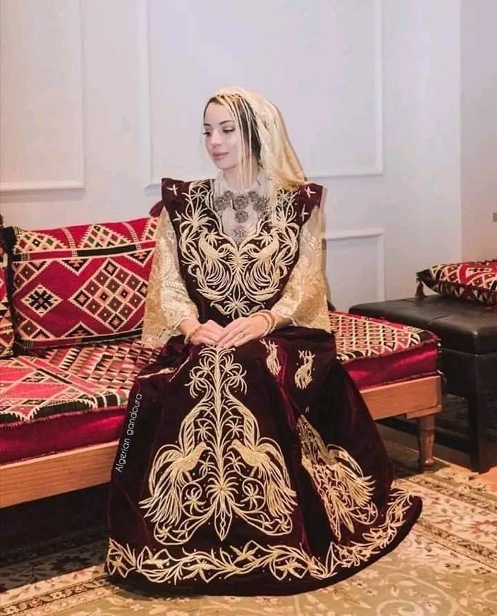 Aicha_Hmr's tweet image. Mariée algérienne portant une très belle gandoura en velours rouge brodée au fil d'or selon la technique #mejboud, C'est une tenue citadine des villes de l'est comme Annaba et Constantine, portée avec des manches amples dorées appelées #kmem et foulard à franges #mharmet_leftoul