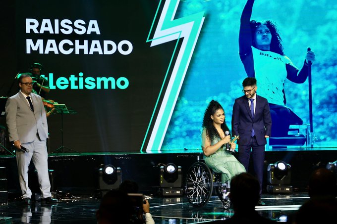Foto da atleta Raissa Rocha Machado, do atletismo, recebendo o prêmio de atleta da galera no palco.