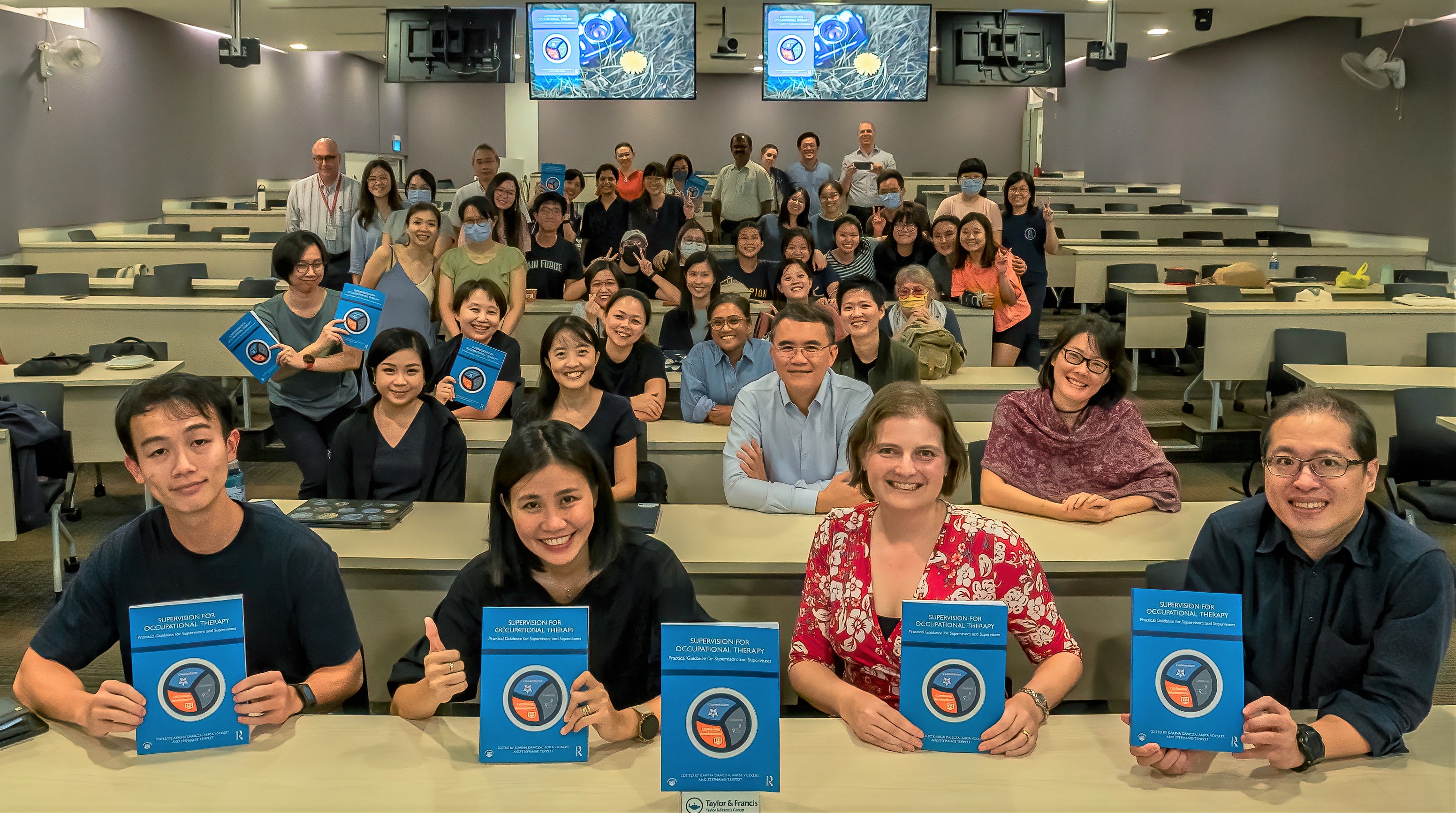 Classroom with a range of people holding the Supervision for Occupational Therapy book