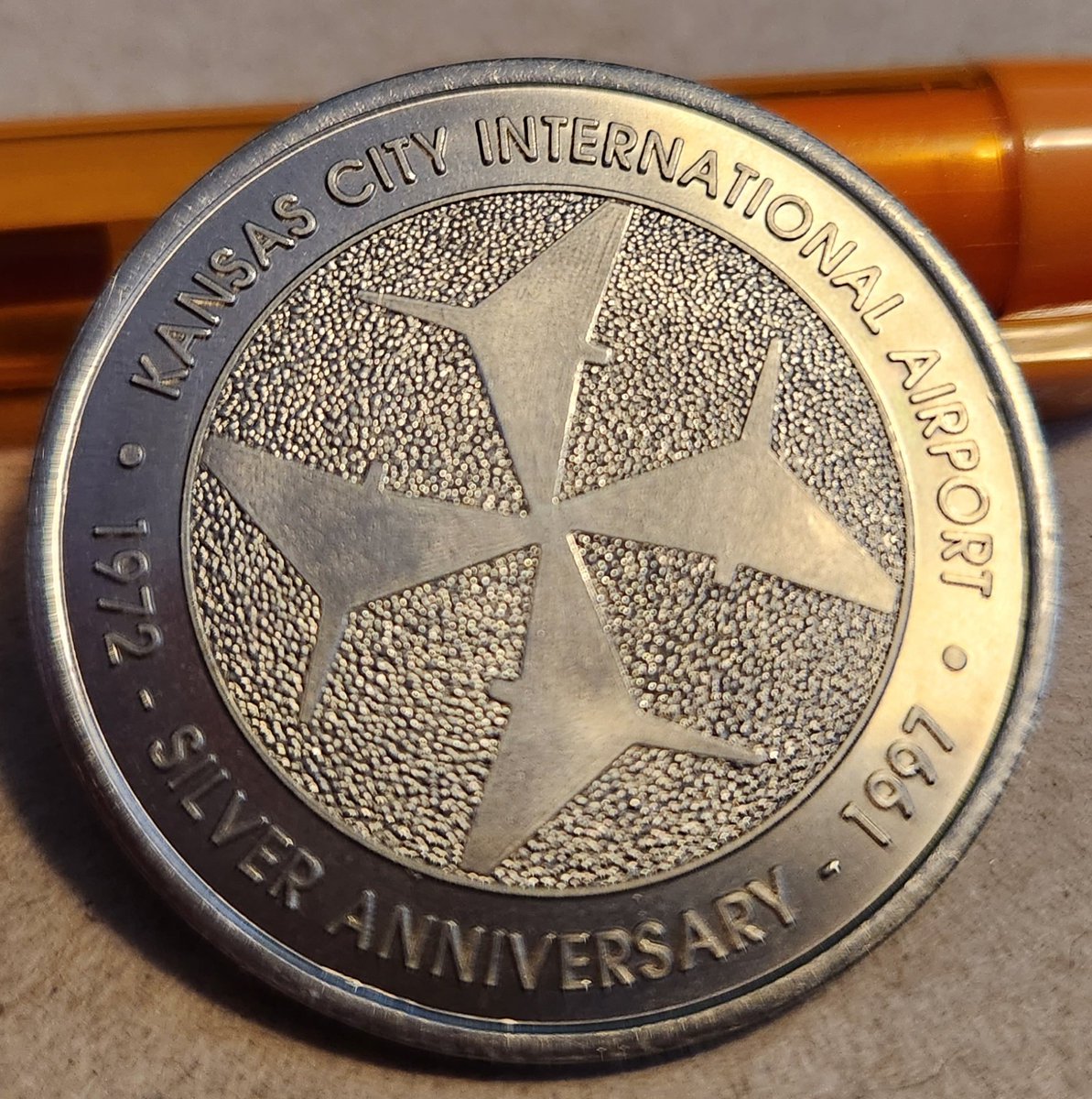 LDKnise's tweet photo. Going through some of parents stuff and came across this little gem. The silver anniversary coin for the current KCI airport.  My Dad worked for Continental Airlines for 34 years.  He worked at the old downtown airport and the current airport.  #FlyKCI #BuildKCI https://t.co/TM6T19kEwL