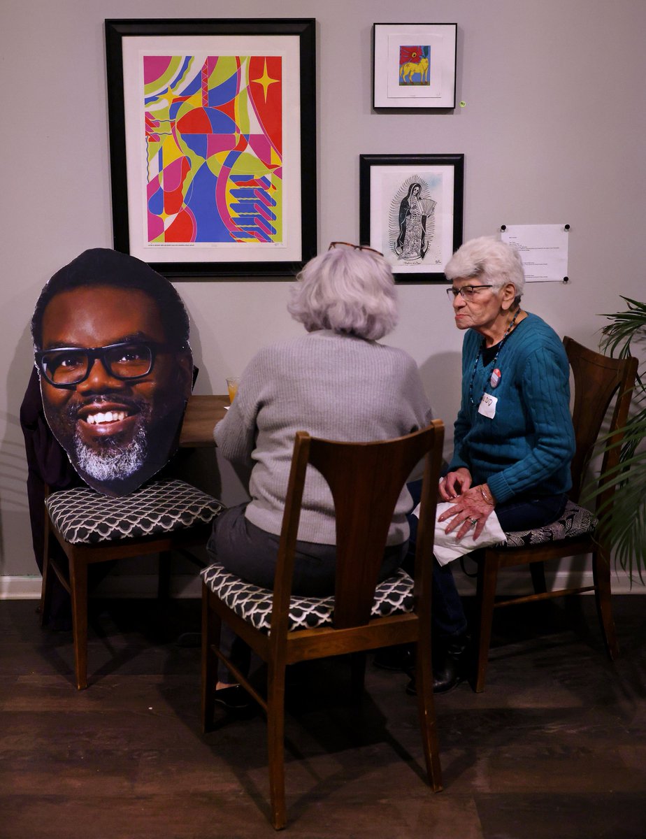 A big head cutout of Chicago mayoral candidate Brandon Johnson rests on a chair as Johnson supporters Sonia Sanchez of Austin and Hilda Frontany (right) of Portage Park snack on empanadas while attending a fundraiser and rally for Johnson in Chicago’s Humboldt Park on Saturday.