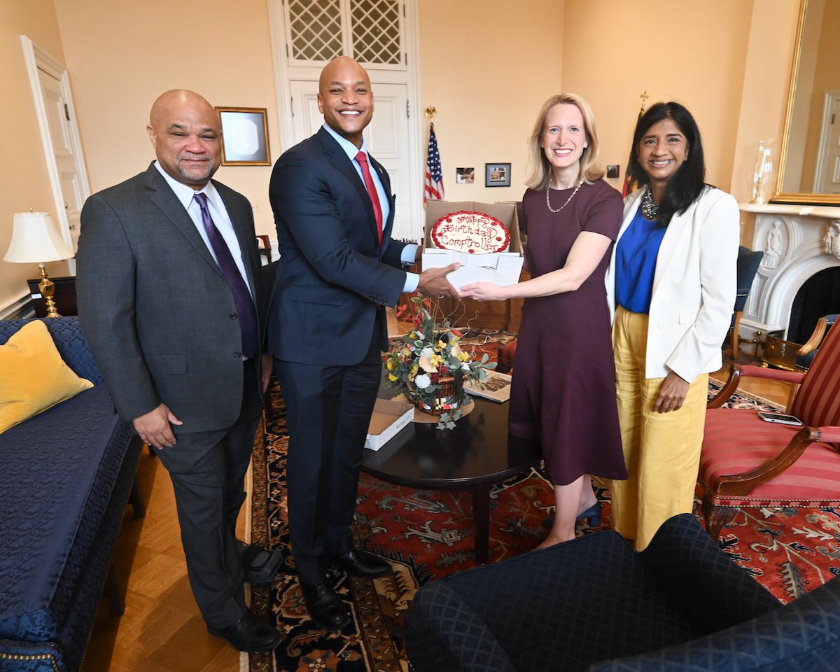 This picture features four people. State Treasurer Dereck Davis, in a dark gray suit and purple tie stands on the far left. On the far right is Lt. Gov. Aruna Miller, who is dressed in a blue blouse, white jacket and yellow pants. In the middle of Davis and Miller stands Gov. Wes Moore, in a navy suit and red tie and Comptroller Brooke Lierman, who is wearing a purple dress. The two are holding a red and white frosted cake that reads, “Happy Birthday Comptroller” in celebration of Comptroller’s birthday, which was on Feb. 14.
