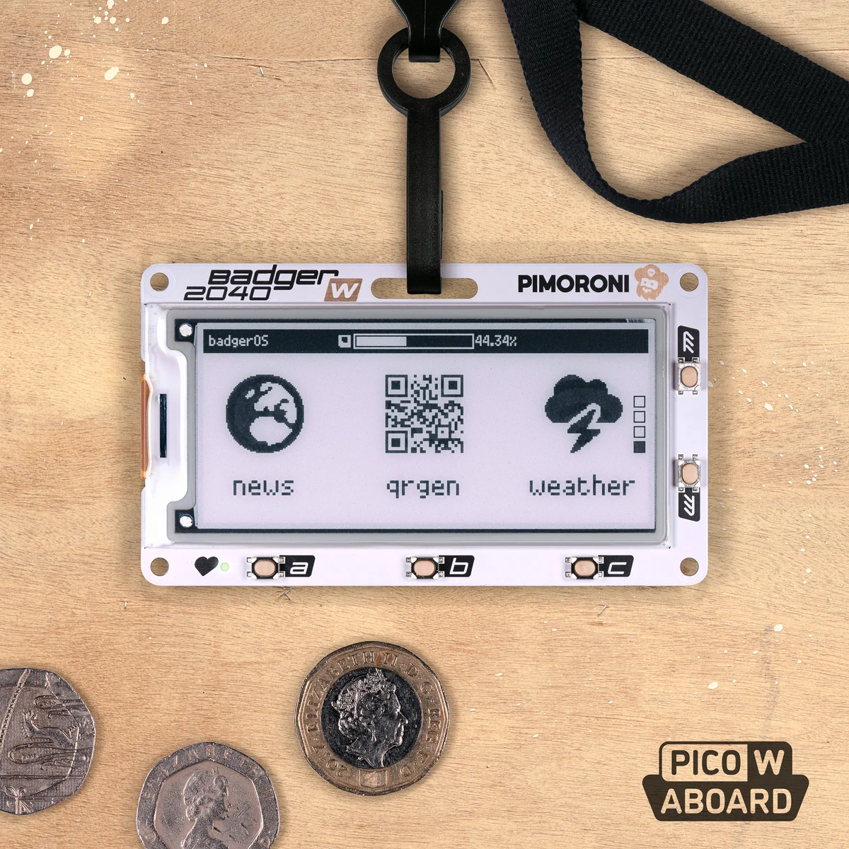 A black and white E Ink badge on a paint splattered wooden background, accompanied by some quaint British coinage.