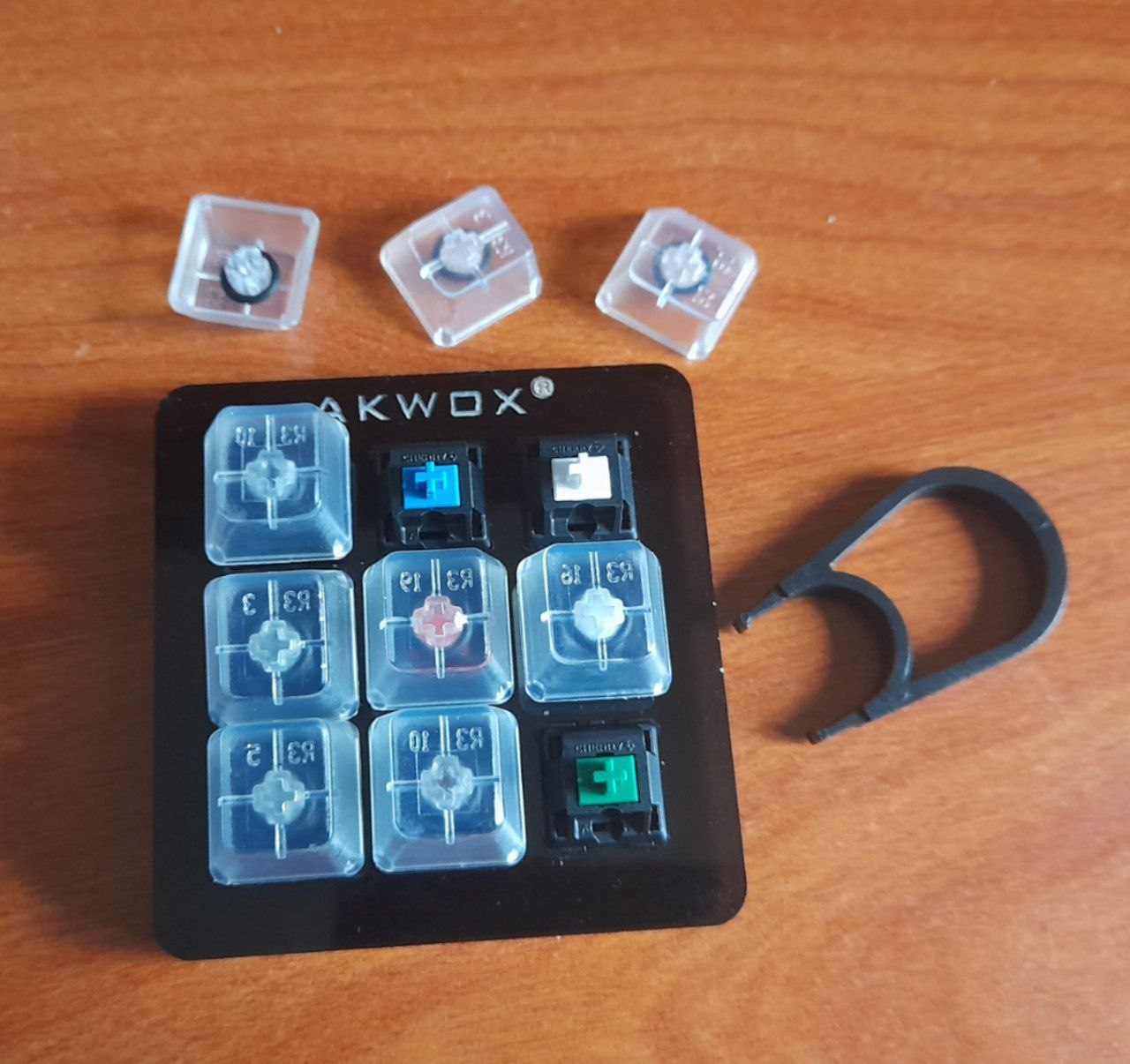 Foto de un panel de nueve teclas (3x3), se trata de un tester para mostrar el funcionamiento de nueve switches diferentes para el periférico. Está sobre una mesa de madera, junto a una herramienta de plástico para extraer las teclas del panel.