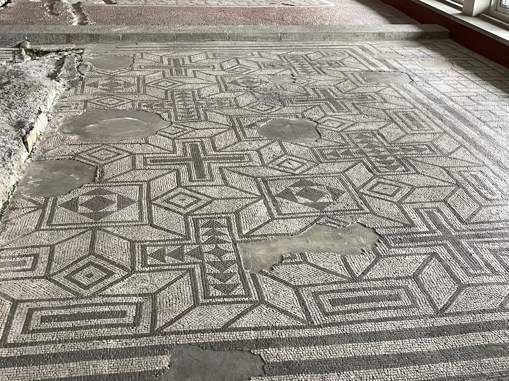 Black on white mosaic with geometric designs. Quite intact but with missing sections here and there.