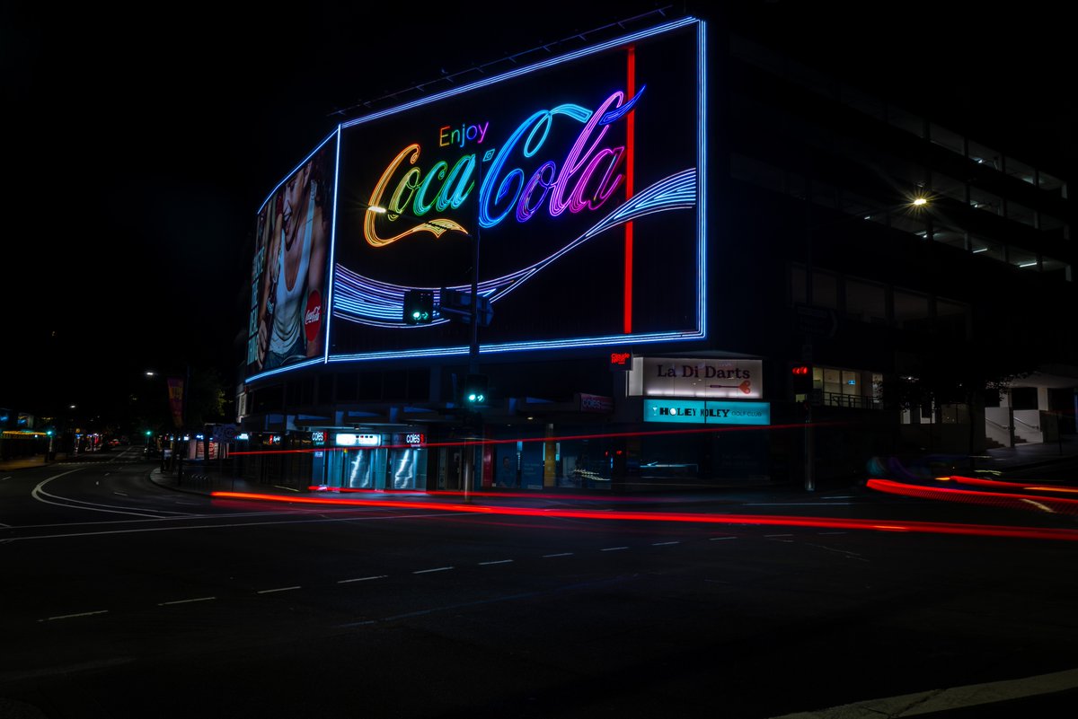 metarand's tweet photo. GM Sydney! Welcome World Pride celebrants. The sun is rising on a cracker of a day #kingscross #kingscrosssydney #worldpride #WorldPride2023 #cokesign #sydney #australia. The Coke sign is usually decked out in the coke red, but is currently resplendent in World Pride Colours https://t.co/t7EKKv6fsU
